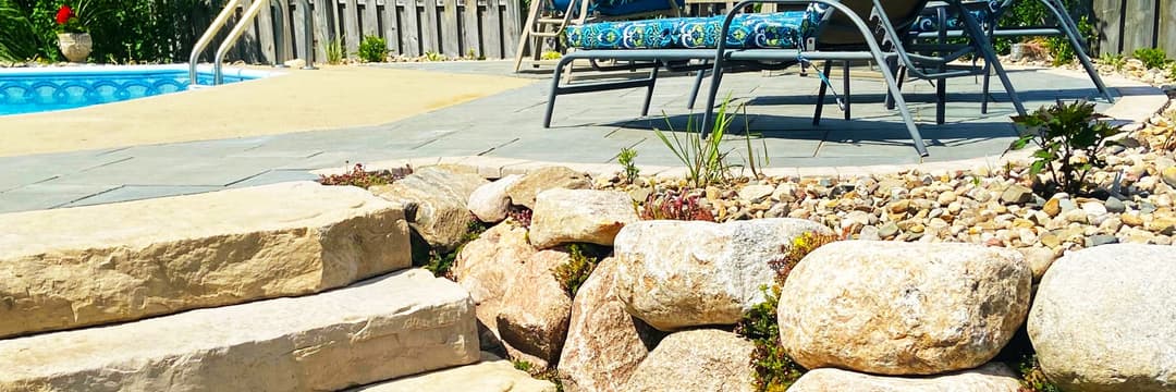 Stone steps lead to a landscaped poolside area with chairs and vibrant greenery.