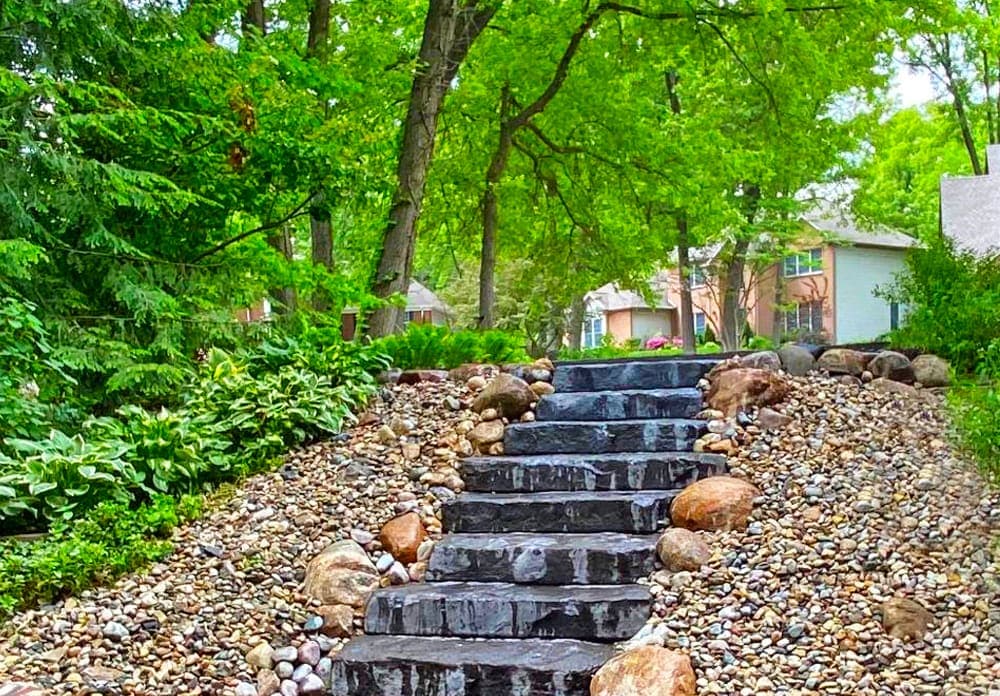 Stone steps leading up a landscaped yard surrounded by greenery and rocks.