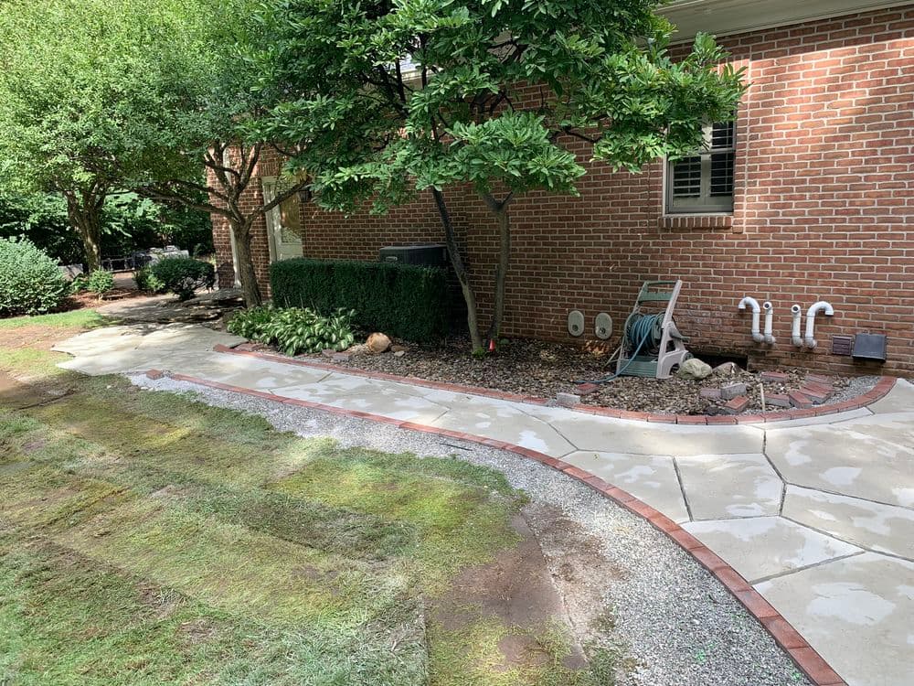 Landscaped backyard with a stone pathway, greenery, and brick trim beside a brick house.