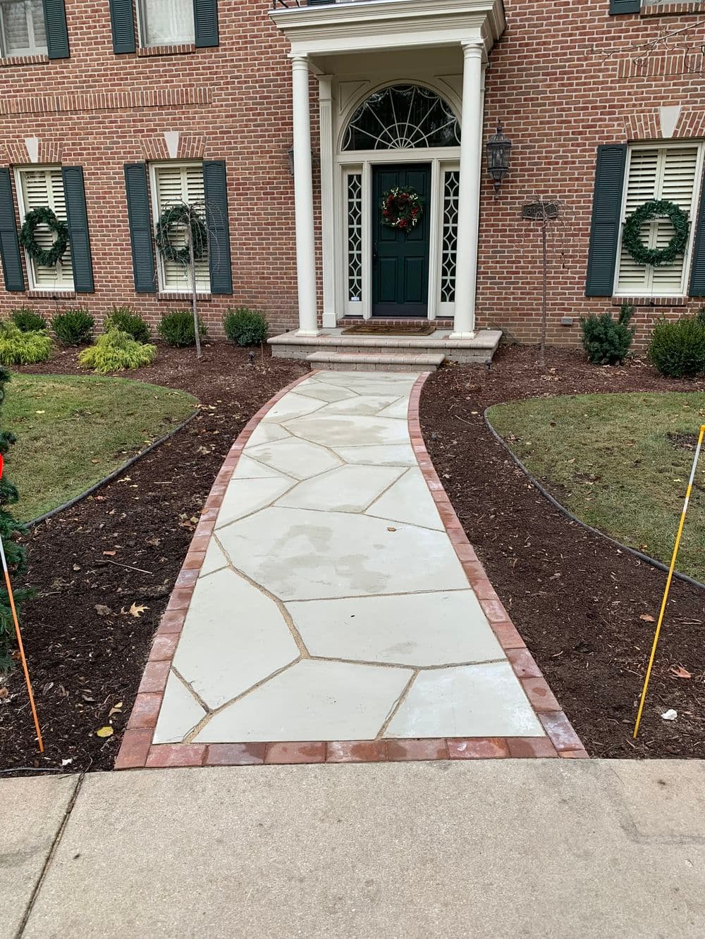 Walkway with decorative stone and brick borders leading to a front door adorned with a wreath.