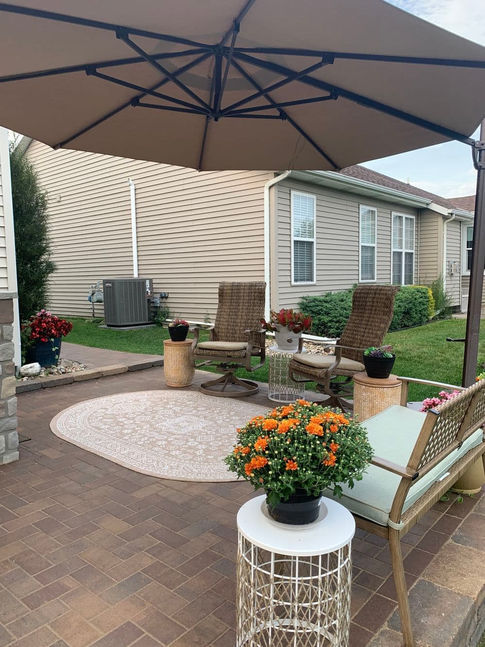Cozy patio area with chairs, table, and vibrant flower pots under a shaded umbrella.