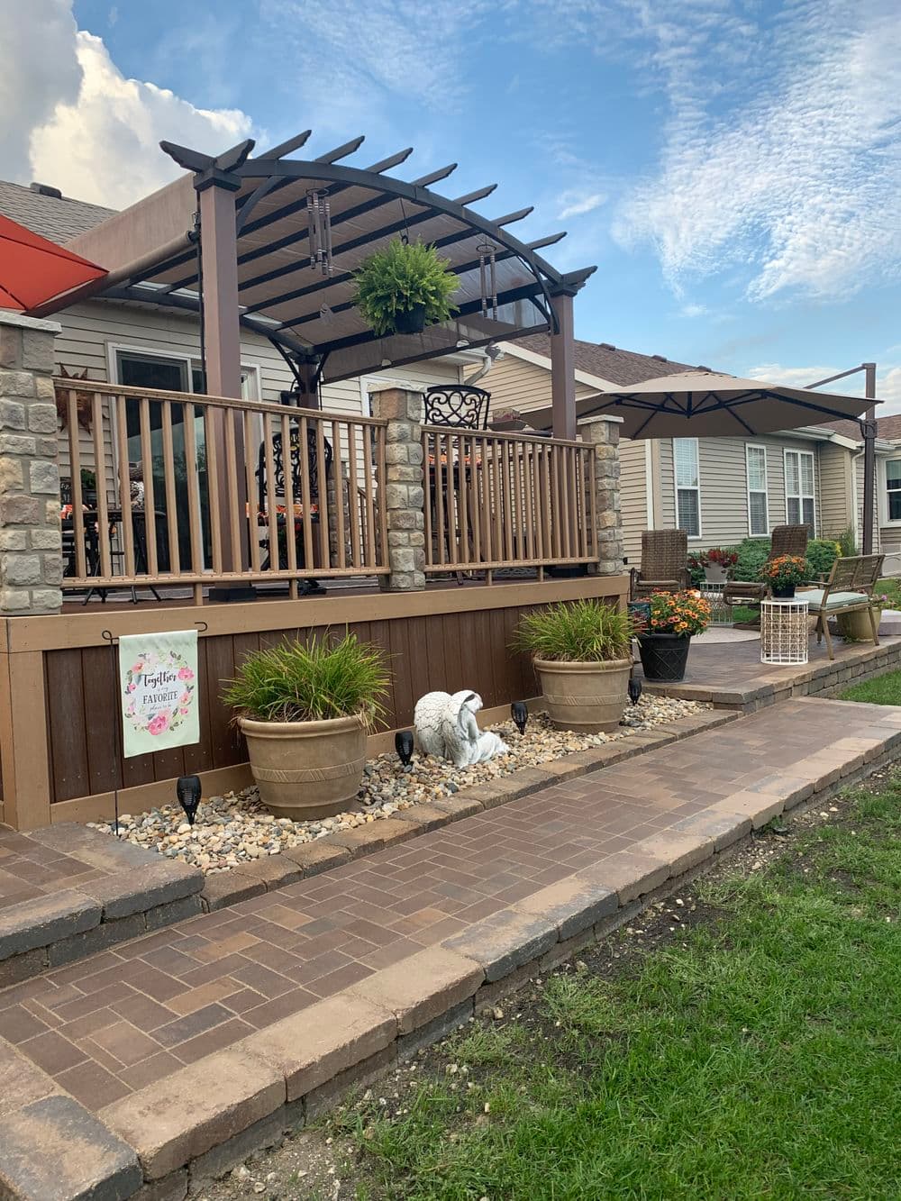 Beautiful outdoor patio with wooden pergola, potted plants, and stone pathway in residential setting.