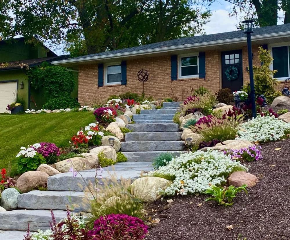 Beautiful landscaped home entrance with stone steps, colorful flowers, and greenery.